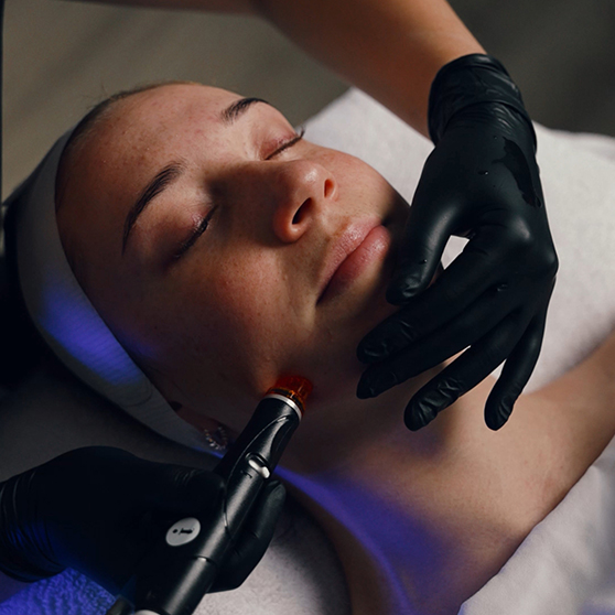 A person receiving a facial treatment with a device on their chin and blue light therapy.